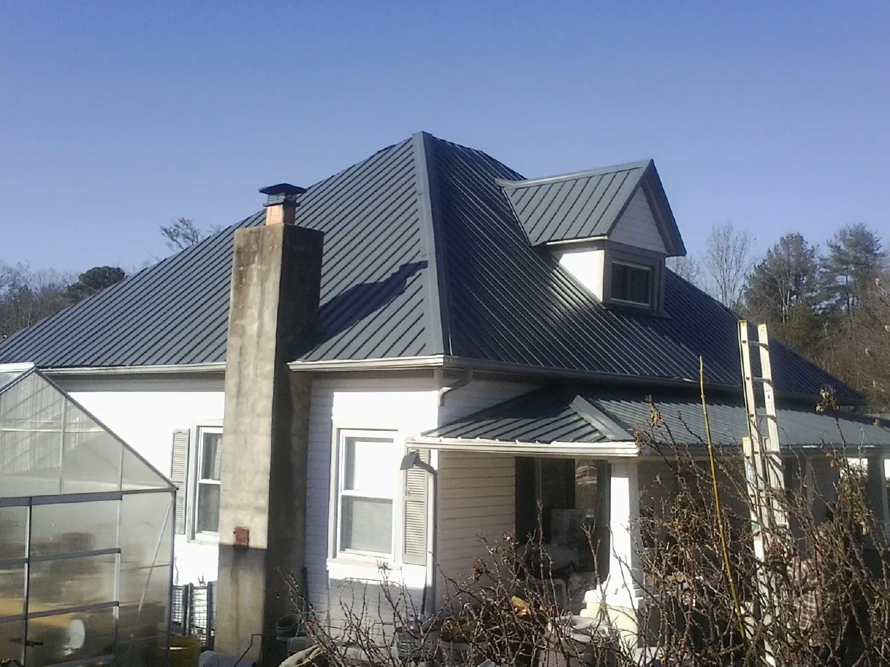 Dark blue standing seam metal roof on a white farmhouse with dormer — Slate & Tile Roof Repair by Roofing Brothers in Schnecksville