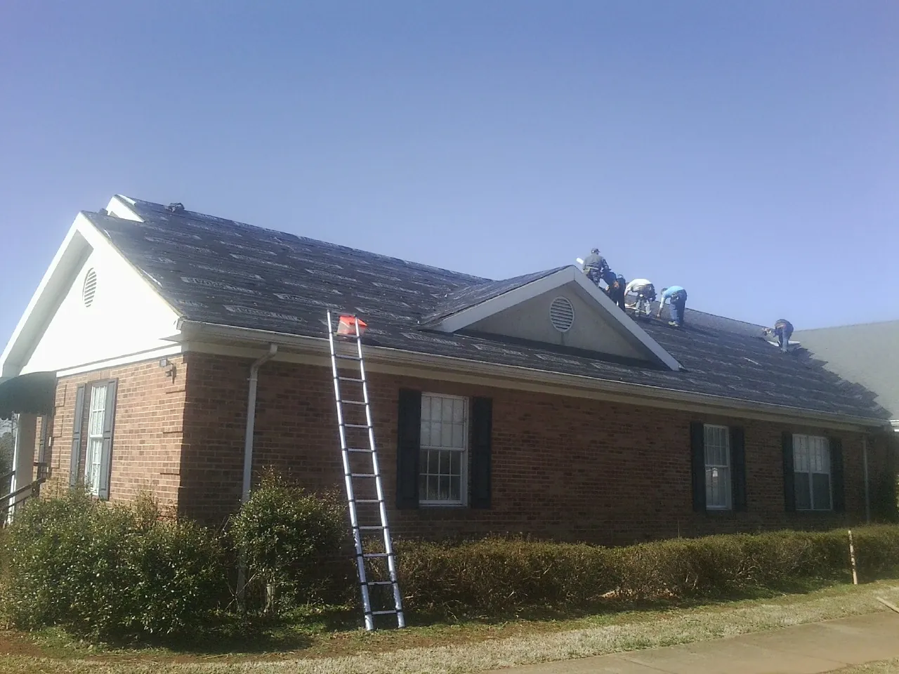 Crew tearing shingles off a brick ranch roof with a ladder set — Emergency Roof Repair work by our crew in Schnecksville