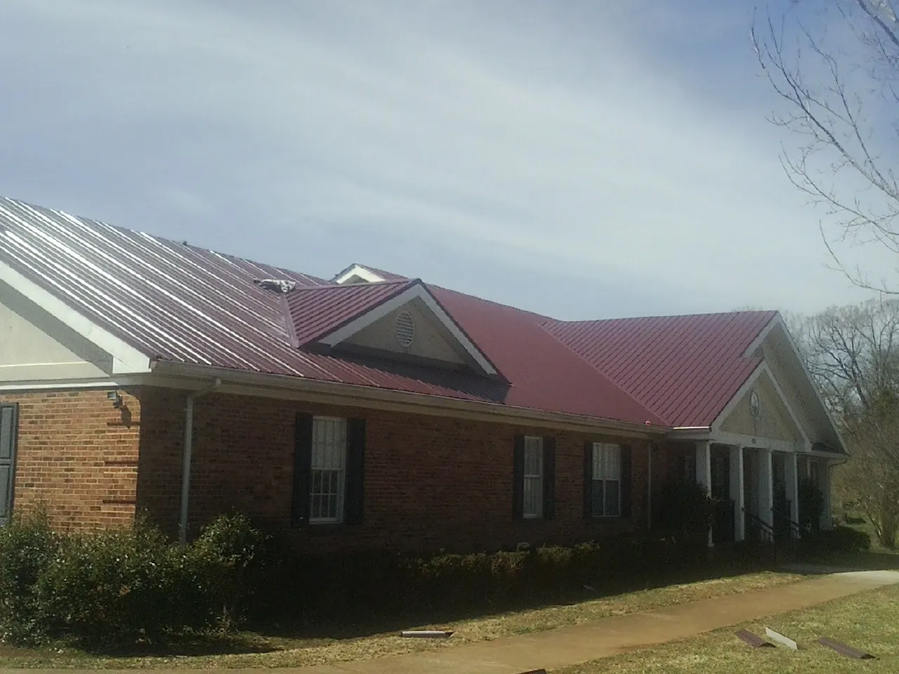 Red metal roof with gabled entries on a long brick building, from a Hail Damage Roof Repair job in Schnecksville