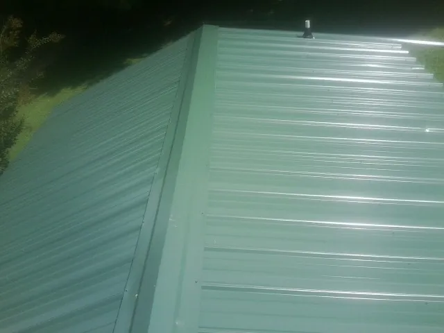 New green metal panels meeting at the ridge of a roof — Flat Roof Repair work by our crew in Schnecksville