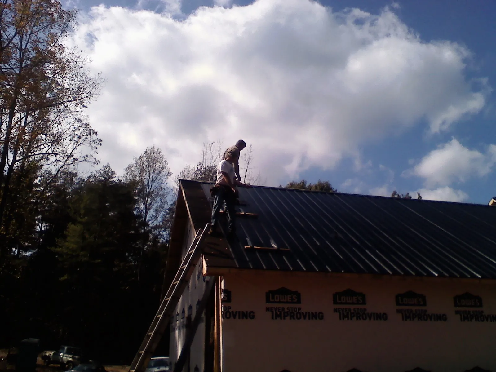 Roofer fastening dark metal panels high against a cloudy sky, from a Roof Inspection job in Schnecksville
