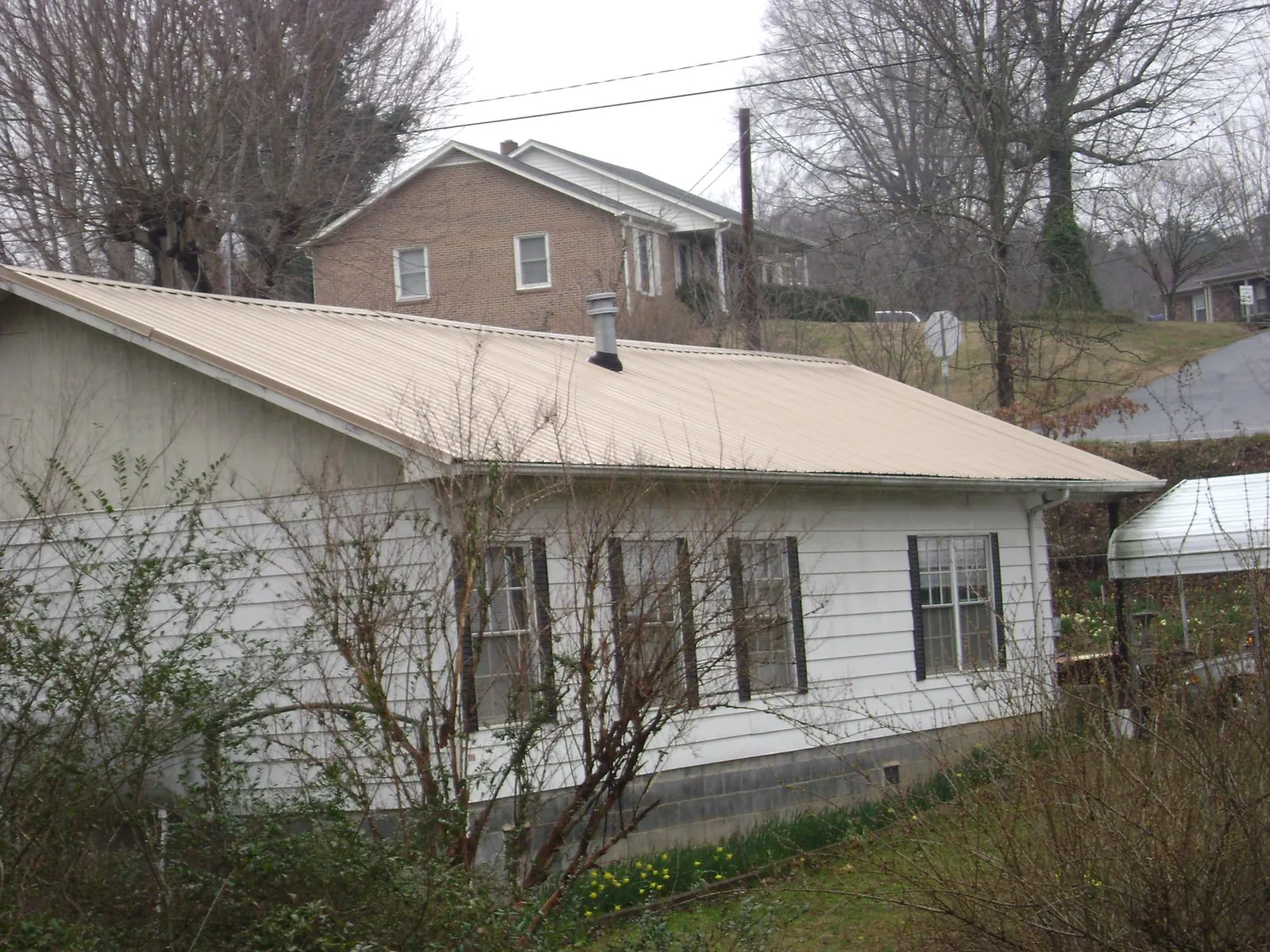 Tan metal roof on a white sided house set into a hillside — Commercial Roofing by Roofing Brothers in Schnecksville